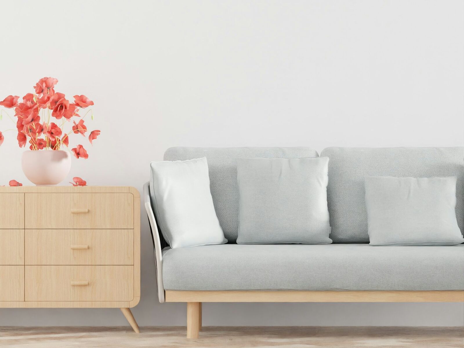 Sala con una cómoda de madera con flores y un sillón gris, con la pared libre